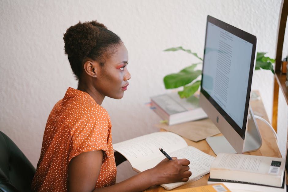 A focused young woman studying with books and a computer at her home office desk